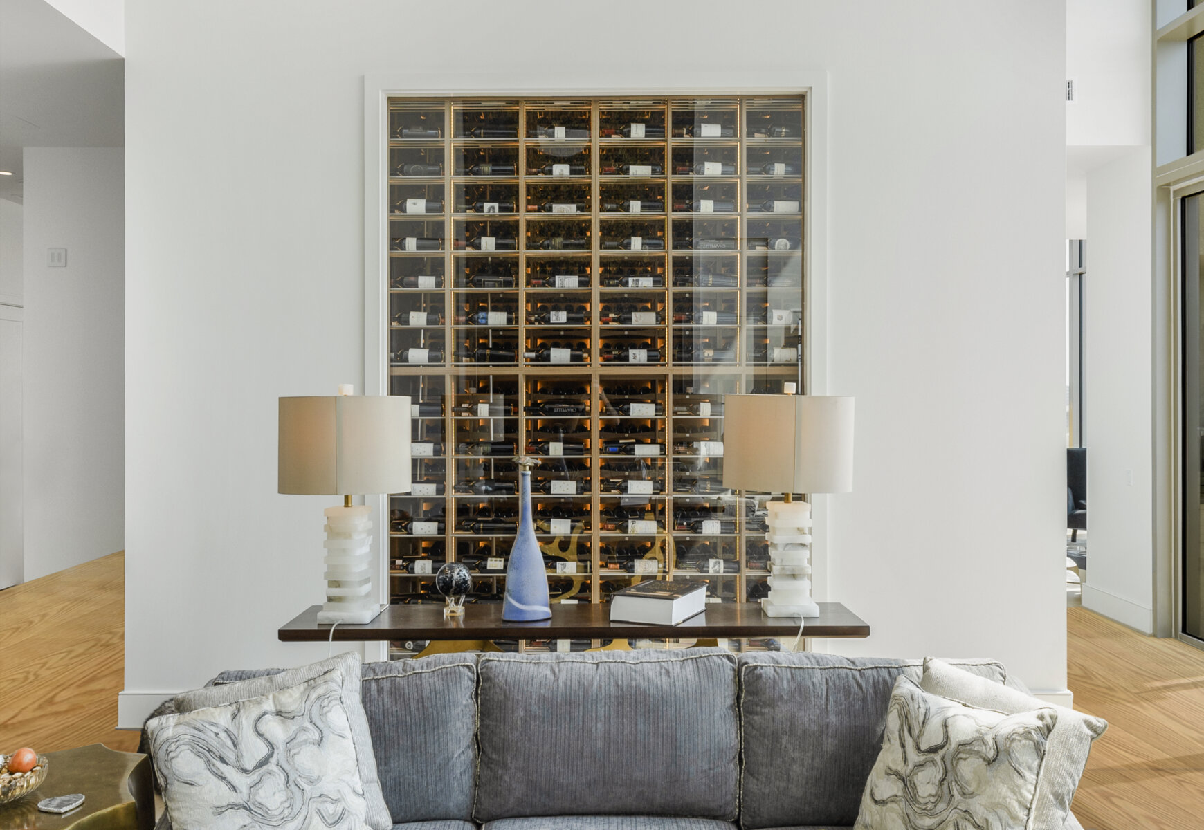 View into modern wine cellar through living room window showing wine bottles displayed on their sides